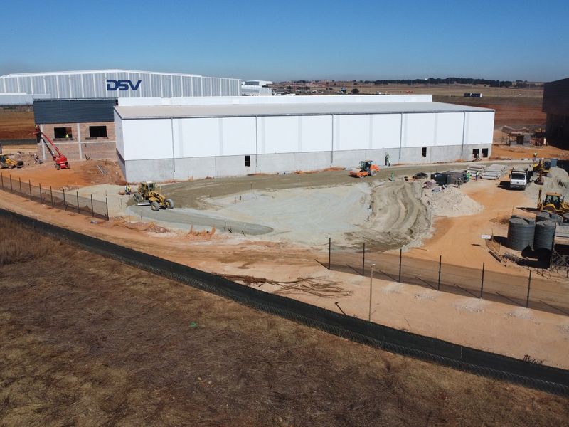 Aerial view of an industrial warehouse facility currently under construction, featuring a large warehouse structure and surrounding unpaved yard area.