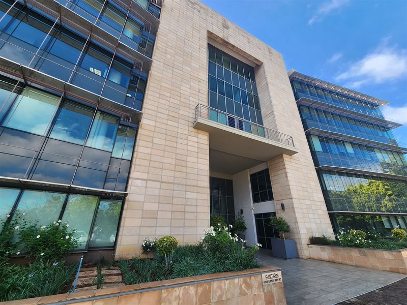 Modern multi-story office building featuring a prominent stone-clad facade, extensive glass curtain walling, and a professional paved entrance area.