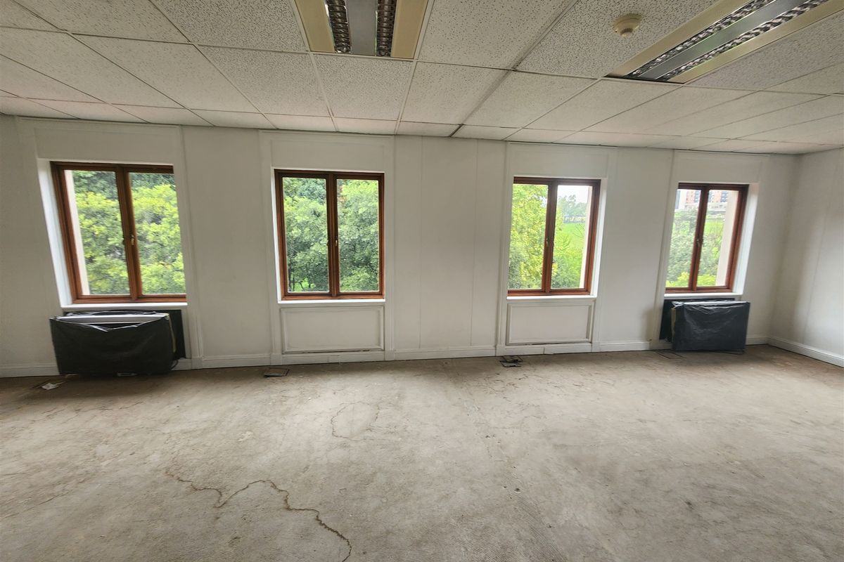 An empty office space featuring large timber-framed windows, suspended ceilings with recessed lighting, and HVAC units, requiring flooring and ceiling refurbishment.