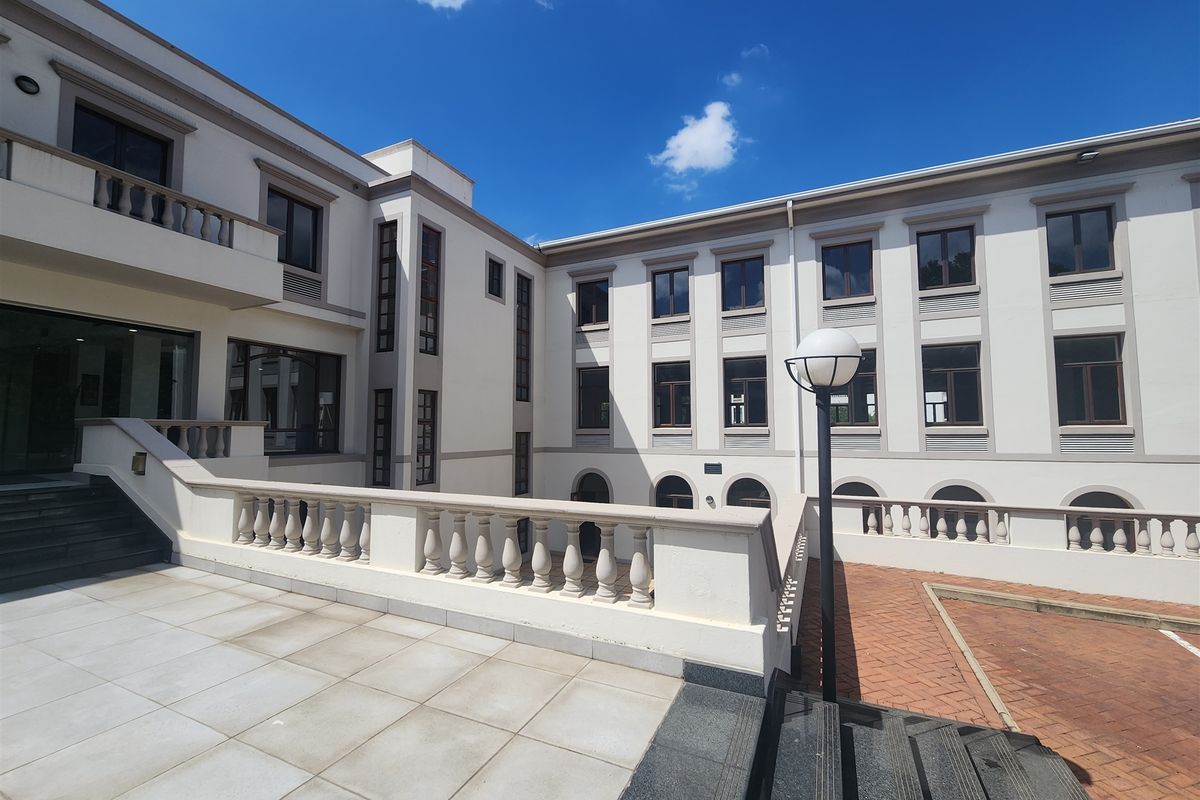 A well-maintained multi-story office building exterior featuring a paved terrace, balustrade detailing, and an external staircase leading to the courtyard area.