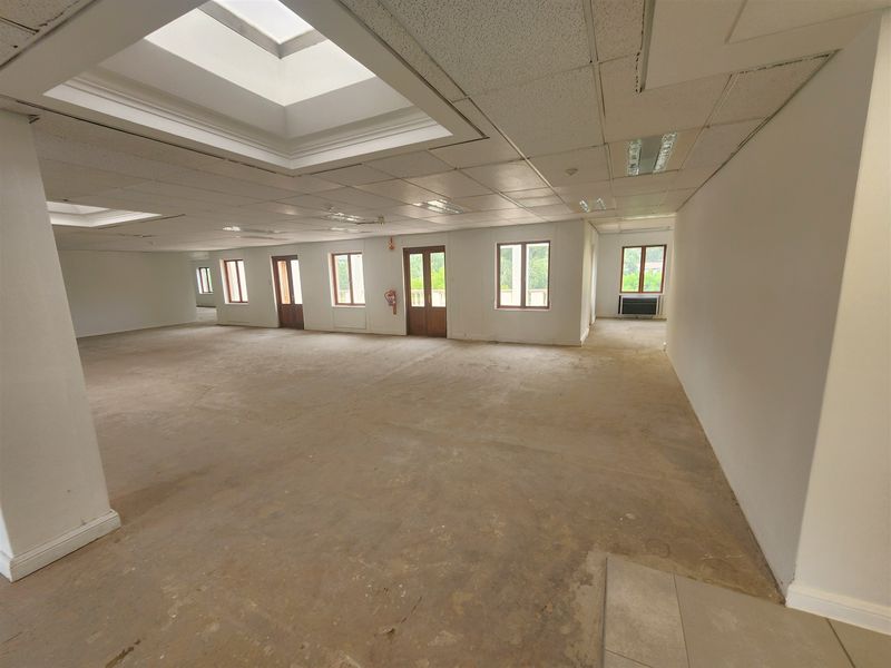 A large, open-plan office space featuring suspended ceilings, multiple skylights, and natural light through wooden-framed windows, currently awaiting flooring and interior finishes.