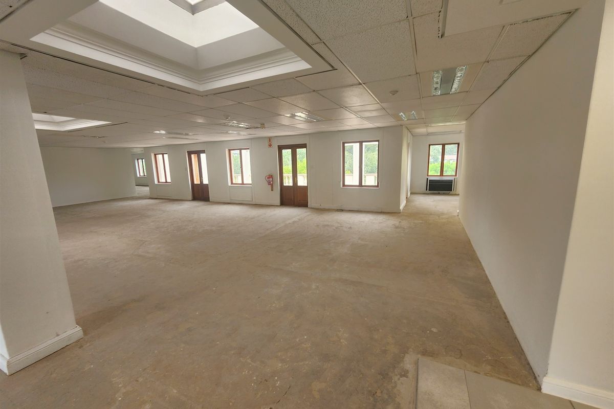A large, open-plan office space featuring suspended ceilings, multiple skylights, and natural light through wooden-framed windows, currently awaiting flooring and interior finishes.