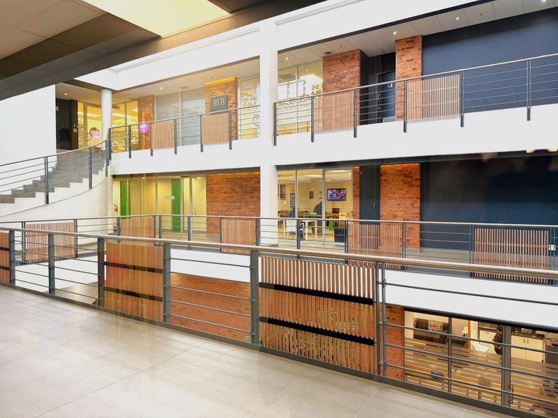 Modern multi-level office atrium featuring exposed brickwork, glass partitions, and contemporary metal and timber balustrades, providing a bright and professional workspace environment.