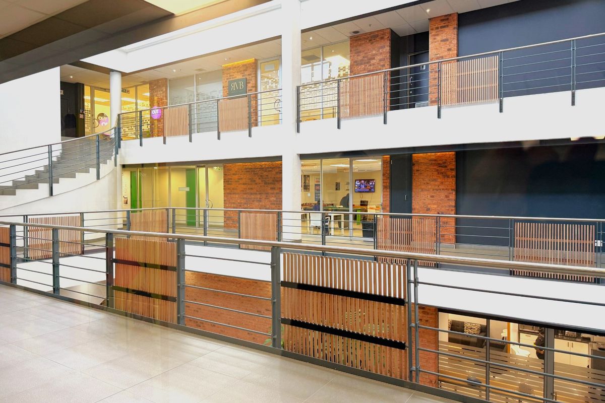 Modern multi-level office atrium featuring exposed brickwork, glass partitions, and contemporary metal and timber balustrades, providing a bright and professional workspace environment.