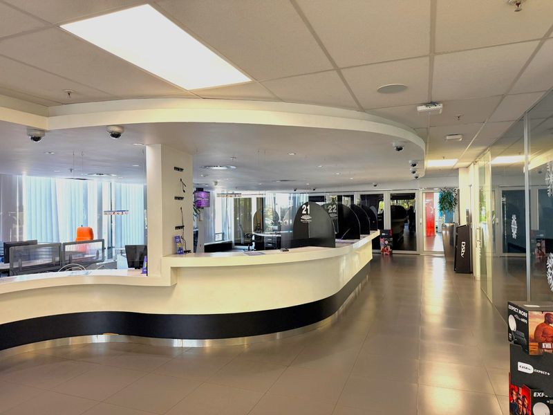 A professional office reception area featuring a large curved service counter, integrated security systems, and modern glass partitions with tiled flooring.