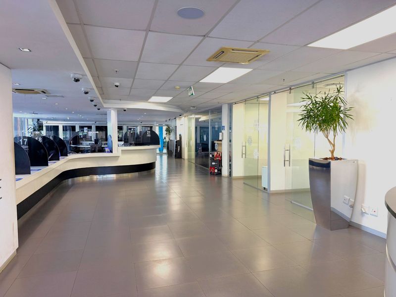 Modern office interior featuring a spacious reception area, tiled flooring, glass-partitioned meeting rooms, and integrated ceiling-mounted air conditioning and security systems.