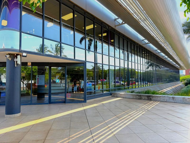 Modern office building exterior featuring a large glass curtain wall facade and a spacious tiled entrance patio area.