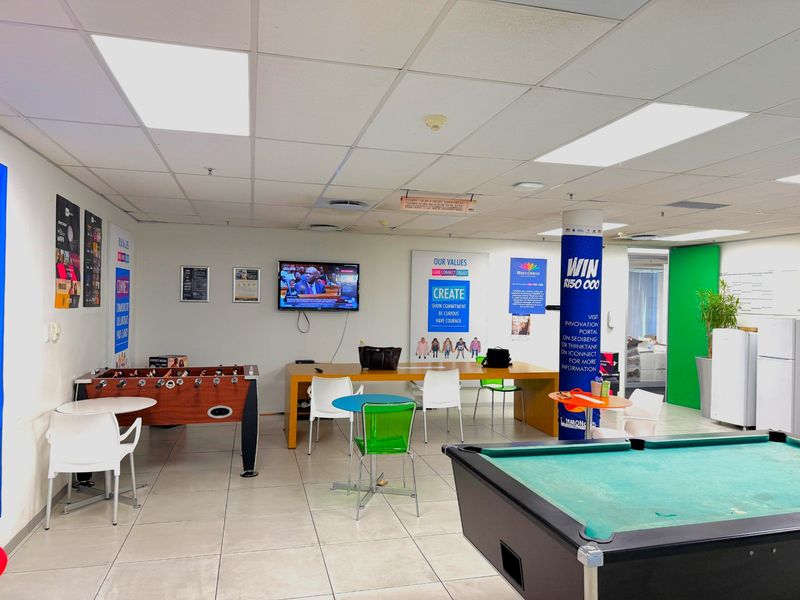 A spacious office breakout area featuring tiled flooring, suspended ceiling with recessed lighting, and integrated air conditioning vents.