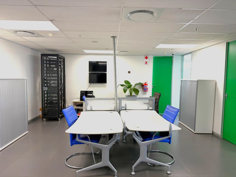 Functional office space featuring a suspended ceiling, tiled flooring, integrated server rack, and built-in storage units, suitable for a professional work environment.