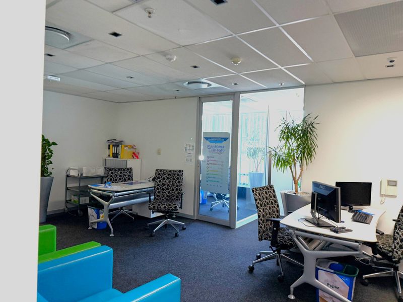 A functional office space featuring a suspended ceiling, recessed lighting, carpeted flooring, and a glass partition door leading to an adjacent area.