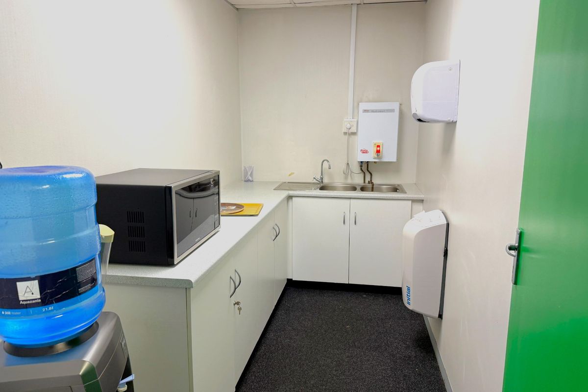 A functional office kitchenette featuring built-in cabinetry, a stainless steel sink, and an instant hot water heater.
