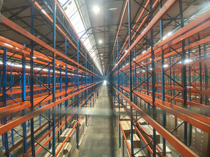 Spacious industrial warehouse interior featuring extensive high-bay pallet racking systems, concrete flooring, and overhead skylights for natural illumination.