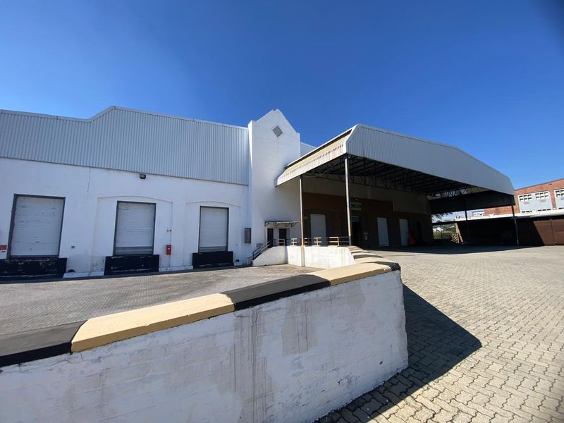 Industrial warehouse exterior featuring a covered loading bay, multiple roller shutter doors, and a paved yard area suitable for logistics operations.