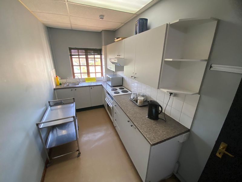 A functional galley-style kitchen featuring built-in cabinetry, laminate countertops, an electric hob, and a stainless steel sink with tiled splashback.