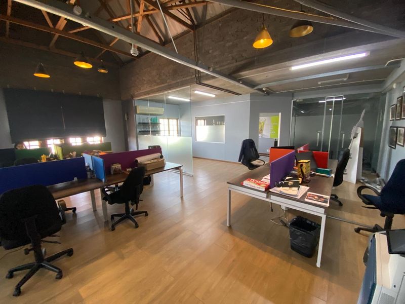 Spacious industrial-style office featuring exposed timber roof trusses, brick walls, and modern glass partitioning, creating an open and collaborative work environment.