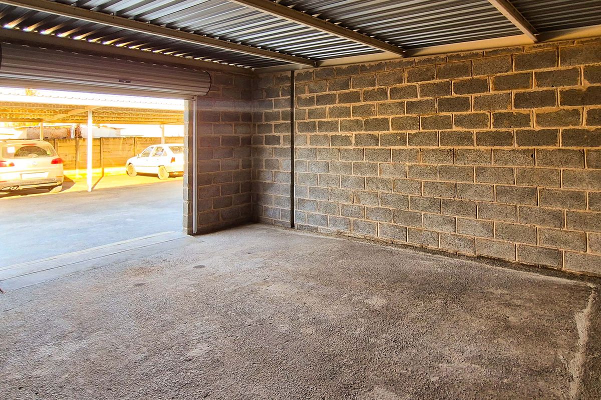 A spacious, empty industrial-style garage featuring exposed concrete block walls, a corrugated metal ceiling, and a functional roller shutter door.