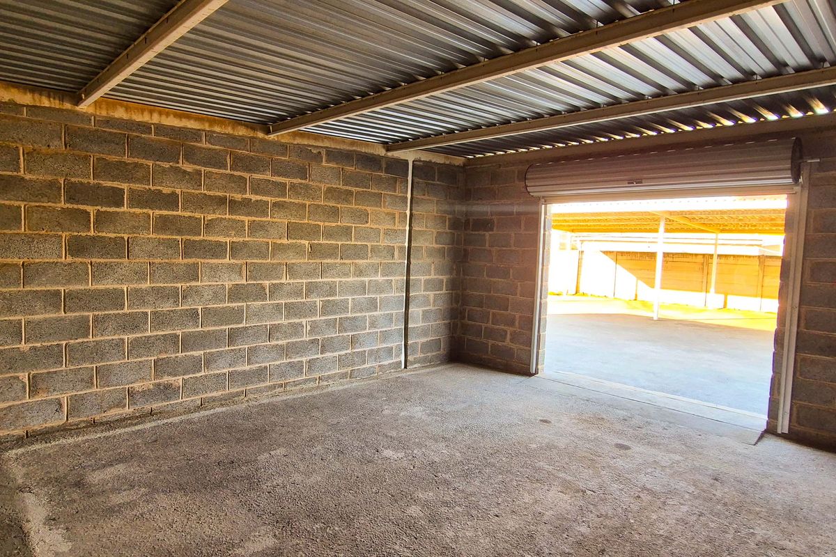 A spacious, empty industrial-style garage featuring exposed concrete block walls, a corrugated metal roof, and a functional roller shutter door.