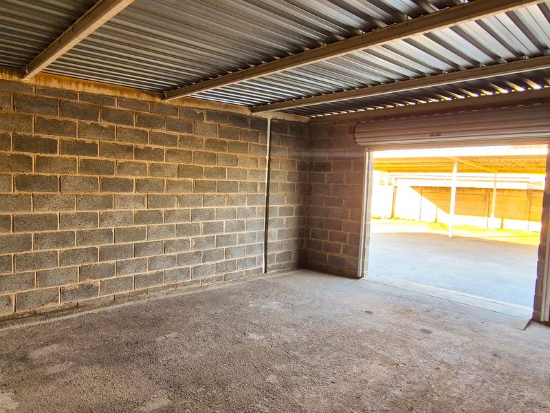 A spacious, empty industrial-style garage featuring exposed concrete block walls, a corrugated metal roof, and a functional roller shutter door.