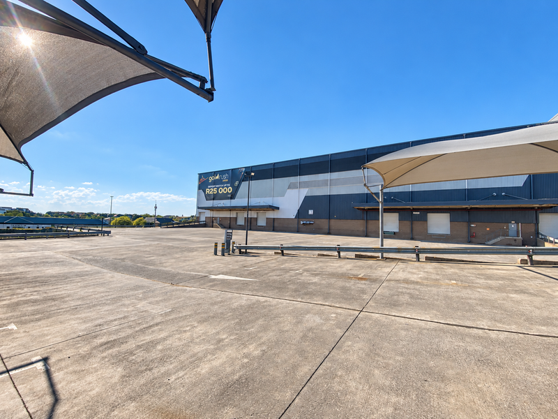 Spacious industrial concrete loading yard featuring multiple loading bay doors, metal cladding facade, and overhead shade sail structures.