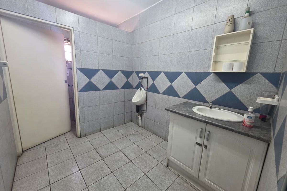 Commercial bathroom featuring a wall-mounted urinal, vanity cabinet with integrated sink, and full-height wall tiling.