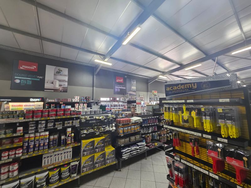 Interior view of a commercial retail space featuring exposed steel roof trusses, fluorescent lighting, and tiled flooring, currently utilized for hardware product display.