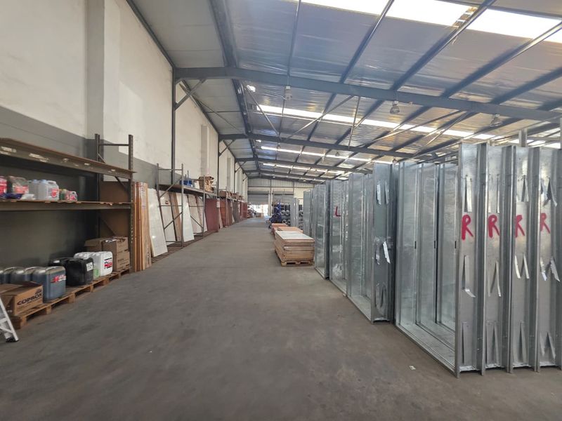 Spacious industrial warehouse featuring high ceilings with integrated skylights, concrete flooring, and extensive built-in steel shelving for storage.