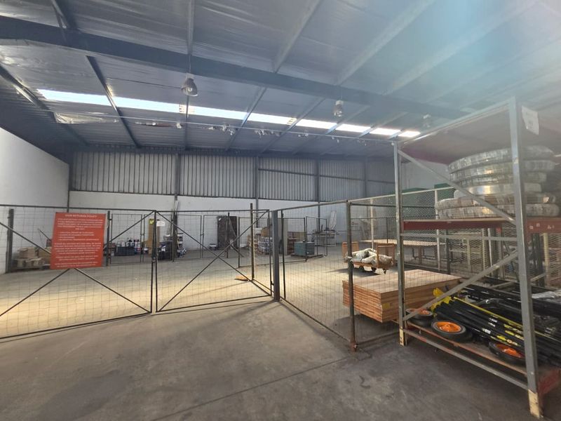 Industrial warehouse space featuring high ceilings with skylights, concrete flooring, and metal partition fencing for secure storage areas.