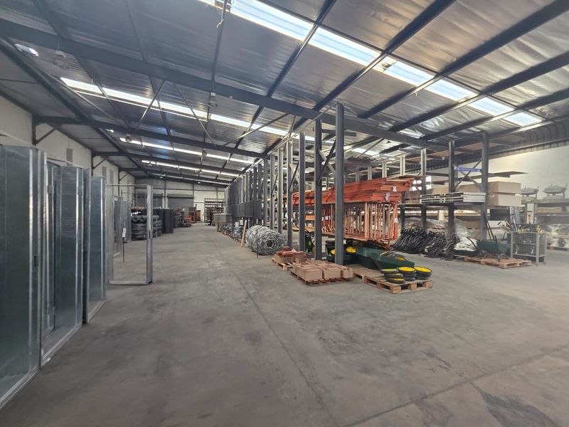 Spacious industrial warehouse featuring high ceilings with integrated skylights, concrete flooring, and extensive steel racking systems for storage.