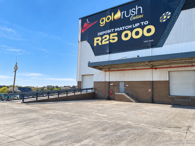 Industrial warehouse exterior featuring a large concrete loading area, roller shutter doors, and a prominent advertising billboard on the building facade.