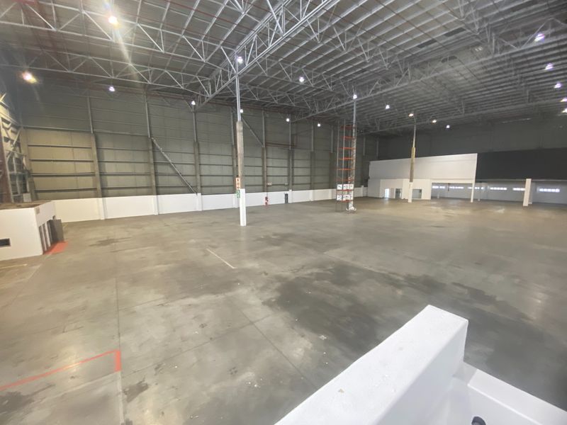Expansive industrial warehouse space featuring high ceilings with exposed steel trusses, polished concrete flooring, and high-bay lighting, suitable for logistics or manufacturing operations.