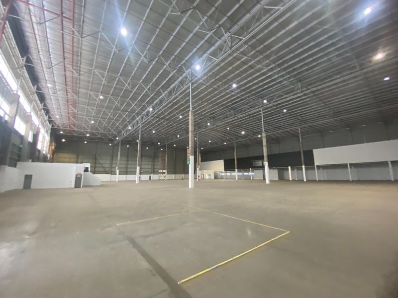 A large, open-plan industrial warehouse space featuring high ceilings with exposed steel trusses, polished concrete flooring, and high-bay lighting throughout.