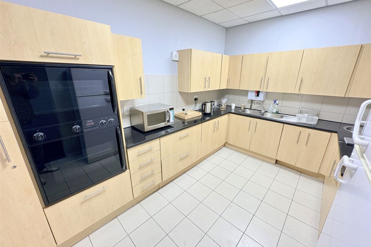 A functional office kitchen featuring light wood cabinetry, black granite countertops, a built-in oven, and tiled flooring.