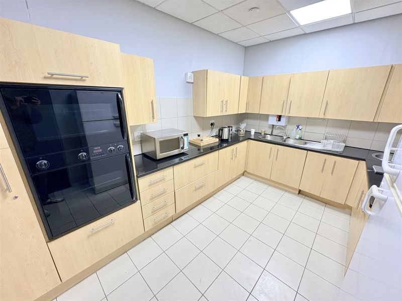 A functional office kitchen featuring light wood cabinetry, black granite countertops, a built-in oven, and tiled flooring.