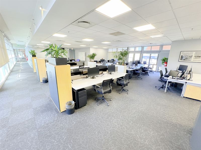 A spacious, well-lit open-plan office area featuring modern workstations, suspended ceilings, and carpeted flooring, suitable for a professional corporate environment.