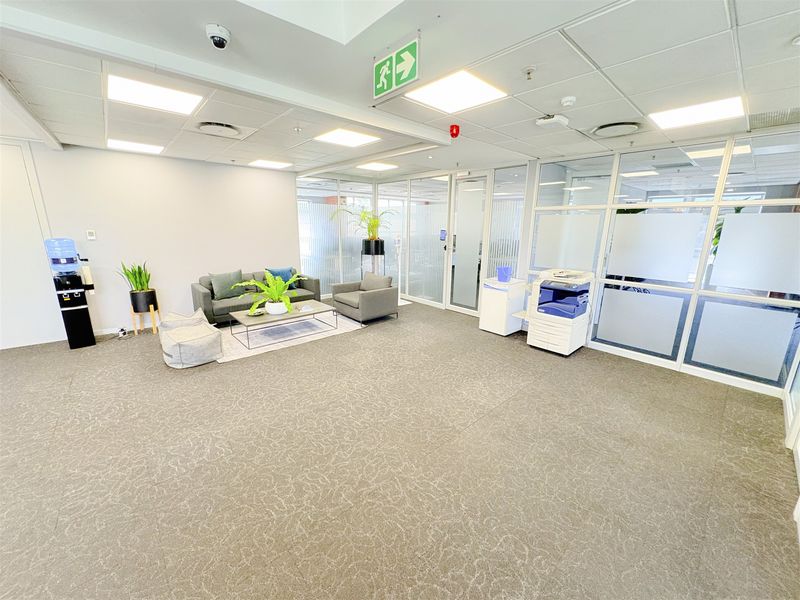 A modern open-plan office space featuring glass partitions, suspended ceilings with recessed lighting, and neutral carpeting, providing a professional and bright work environment.