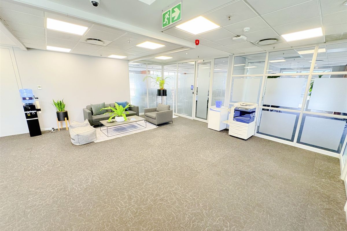 A modern open-plan office space featuring glass partitions, suspended ceilings with recessed lighting, and neutral carpeting, providing a professional and bright work environment.