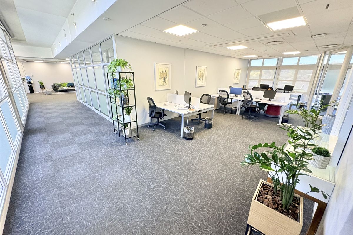 A bright, open-plan office space featuring modern glass partitions, suspended ceilings with recessed lighting, and large windows providing ample natural light.