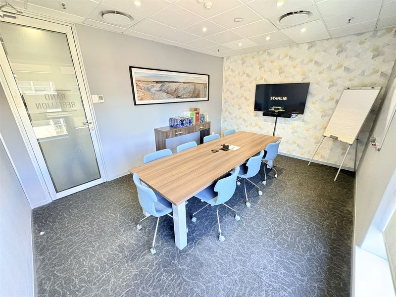 A professional office meeting room featuring a suspended ceiling, recessed lighting, patterned accent wall, and glass entry door.