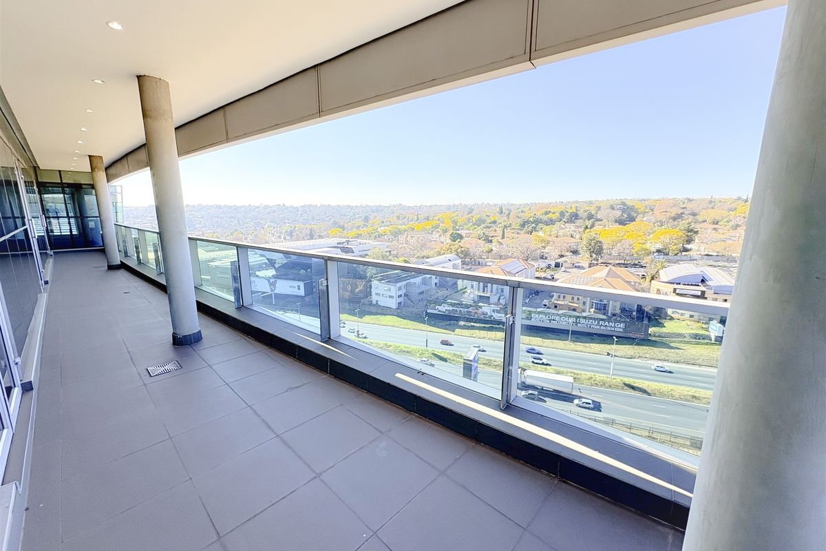 A spacious, modern covered balcony featuring tiled flooring, structural support columns, and a glass balustrade offering expansive elevated views.