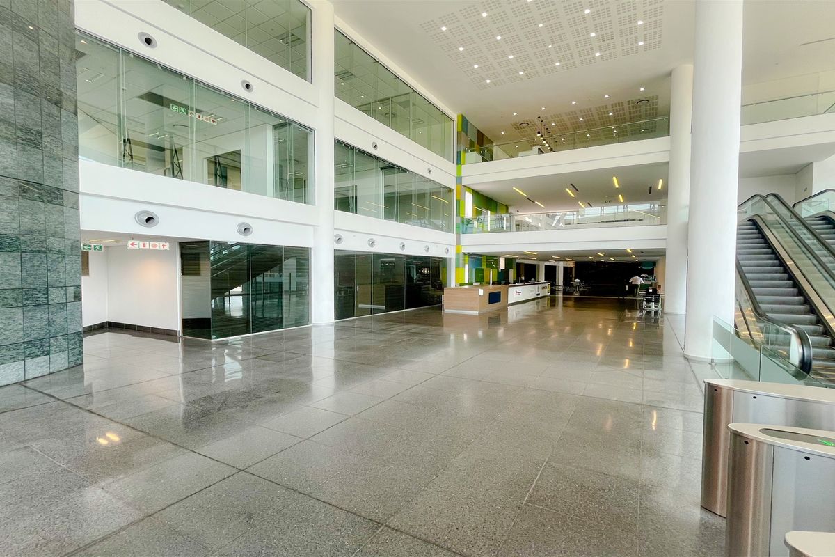 Spacious modern office building atrium featuring polished stone floors, glass-walled office suites, a central reception area, and an escalator for multi-level access.