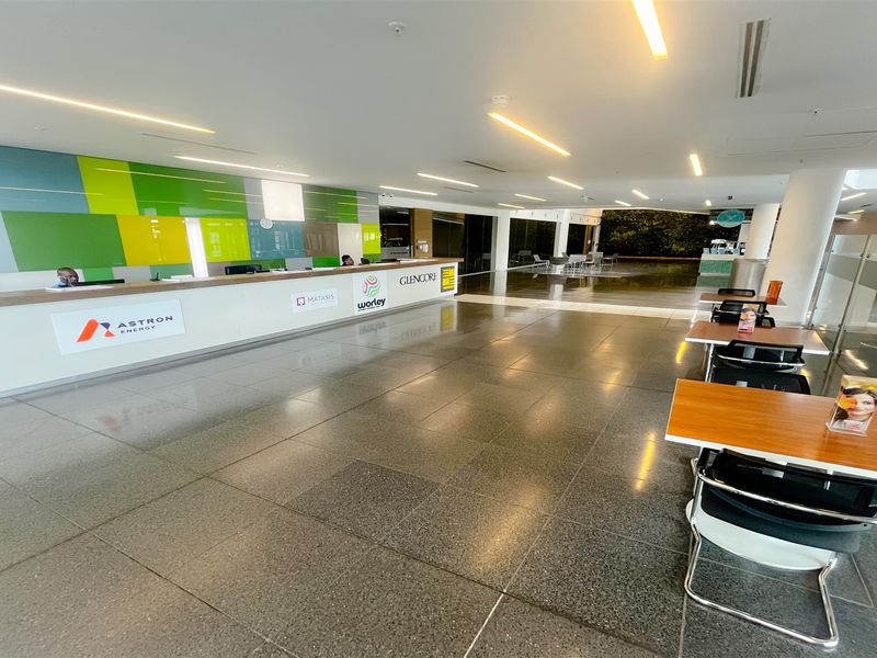 Spacious modern office reception area featuring a long reception desk, polished stone flooring, recessed linear lighting, and a decorative vertical garden wall.