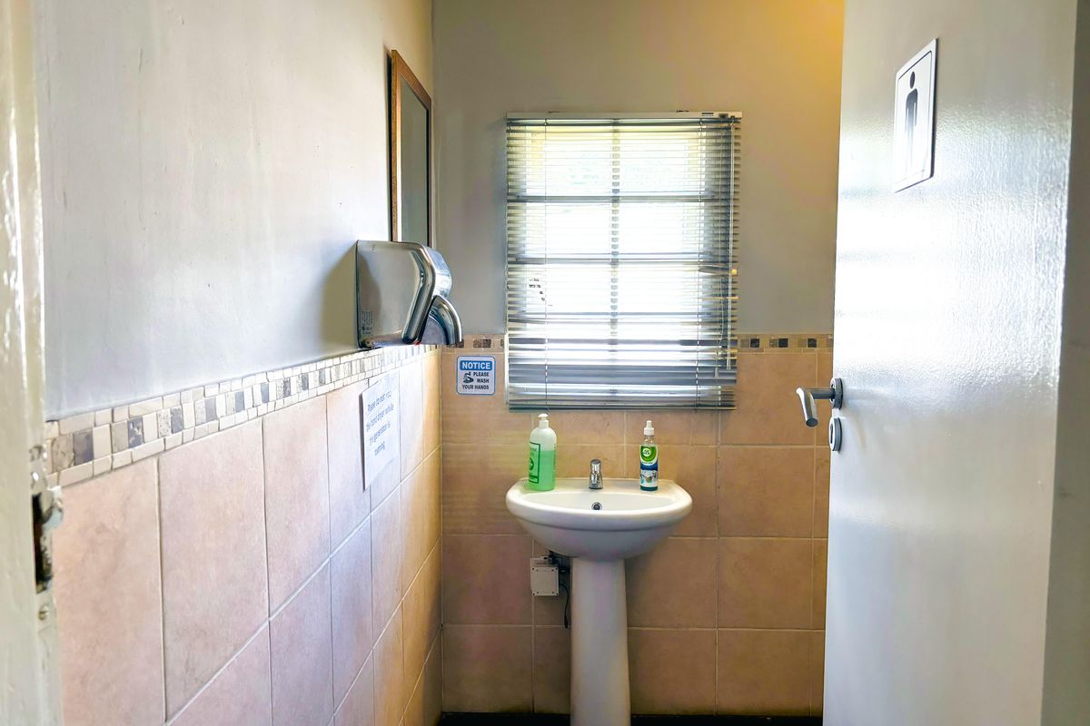 A functional commercial restroom featuring a pedestal basin, tiled splashback, and wall-mounted hand dryer.
