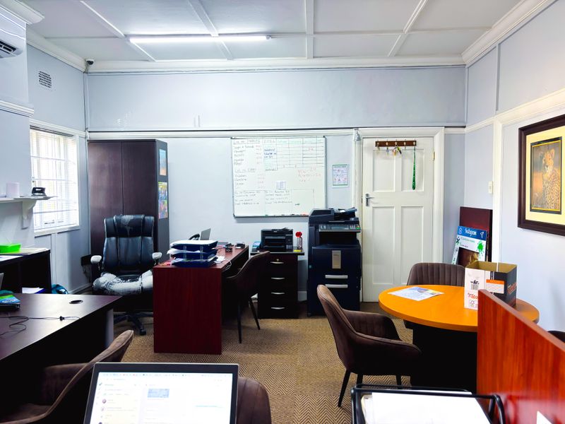A functional commercial office space featuring carpeted flooring, a tiled ceiling, and secure window bars, suitable for a professional work environment.
