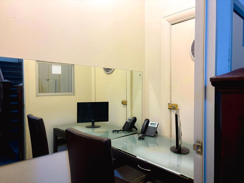 A compact office space featuring a large wall-mounted mirror, internal door, and ventilation fan, suitable for a small workstation or administrative area.
