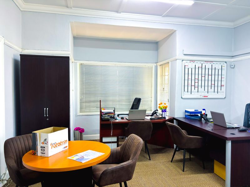 A functional commercial office space featuring carpeted flooring, built-in storage cabinetry, and large windows with venetian blinds for natural light control.