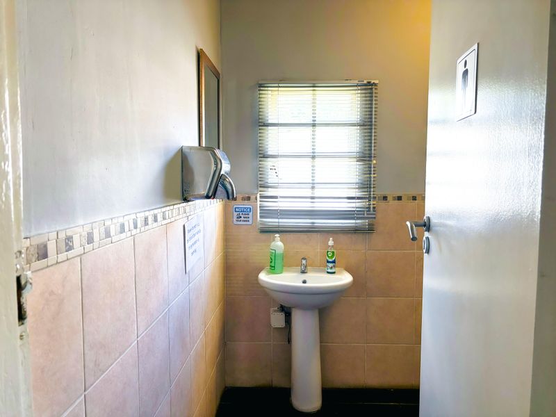 A functional commercial restroom featuring a pedestal basin, tiled splashback, and wall-mounted hand dryer.