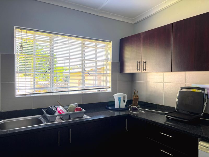 A functional kitchen area featuring dark cabinetry, granite countertops, a stainless steel sink, and a tiled backsplash with natural light from the window.