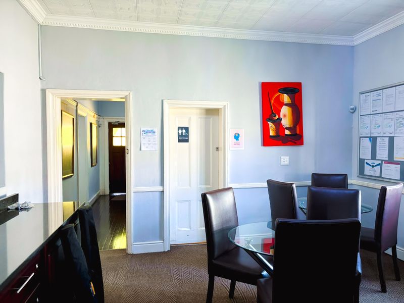 A commercial interior space featuring crown molding, wainscoting, and textured ceiling tiles, providing a functional area with access to internal hallways and restroom facilities.