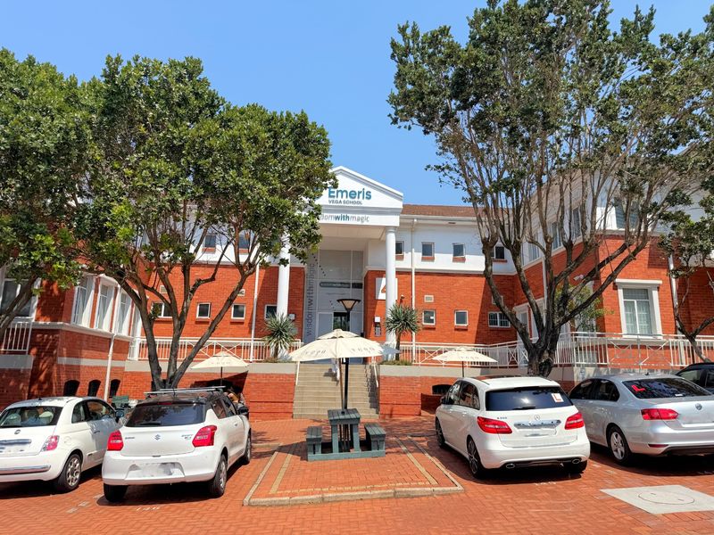 Front elevation of a brick office building featuring a prominent entrance with columns and a pediment, set within a landscaped campus environment.