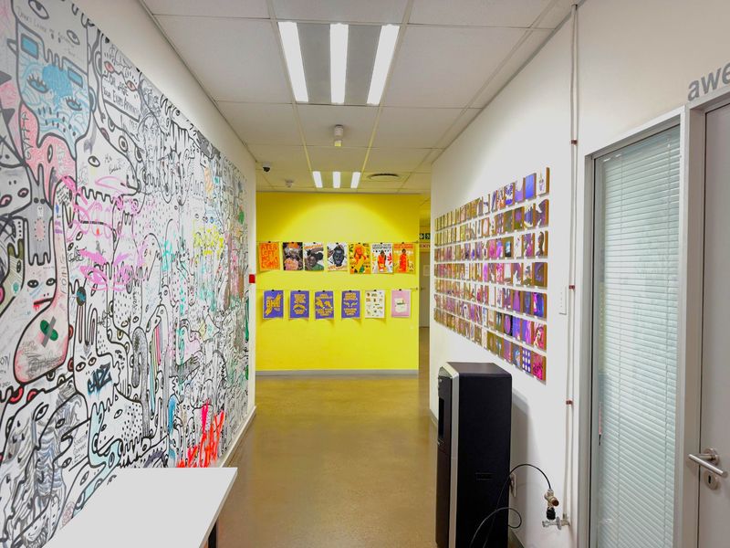 A bright office hallway featuring a suspended ceiling, recessed lighting, and durable vinyl flooring, leading to a vibrant yellow accent wall.